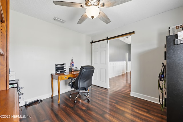 office space featuring visible vents, a ceiling fan, a barn door, and wood finished floors