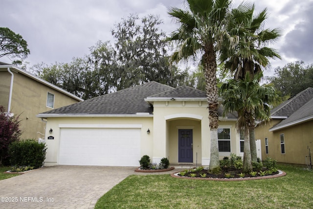 view of front facade featuring decorative driveway, an attached garage, a front lawn, and stucco siding