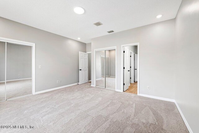 unfurnished bedroom with two closets, baseboards, light colored carpet, and a textured ceiling