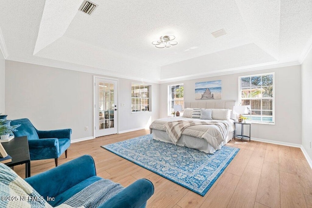 bedroom with a tray ceiling, multiple windows, visible vents, and wood-type flooring