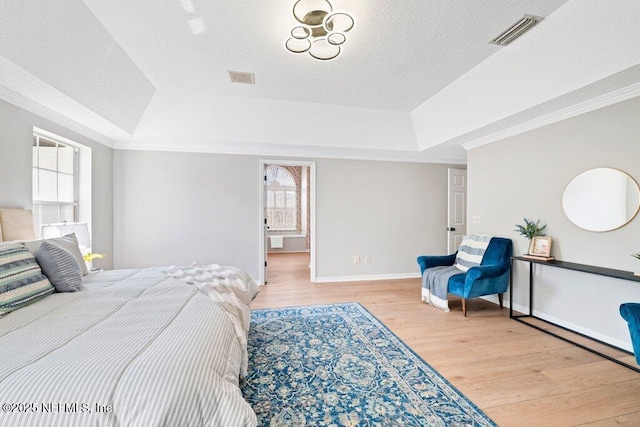 bedroom featuring a tray ceiling, crown molding, visible vents, and light wood-type flooring