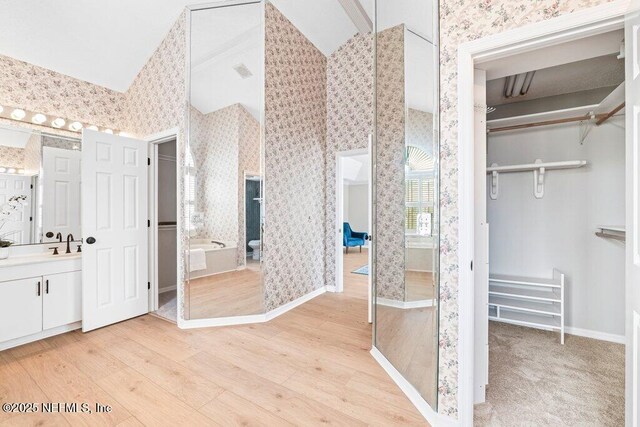 bathroom featuring a walk in closet, vanity, and wallpapered walls