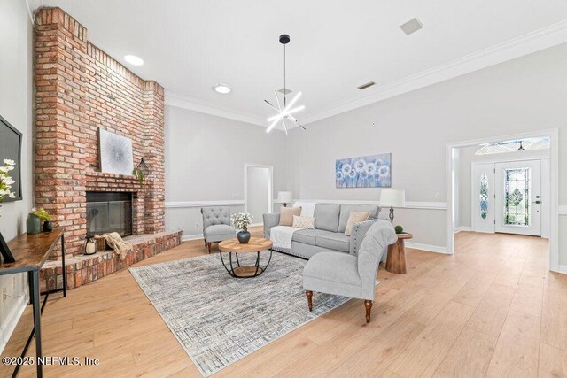 living room with visible vents, a brick fireplace, crown molding, an inviting chandelier, and wood finished floors