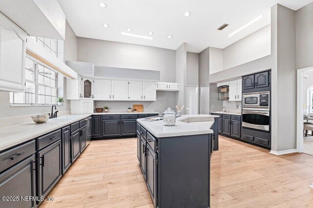 kitchen featuring a sink, a towering ceiling, white cabinets, stainless steel appliances, and a kitchen island with sink