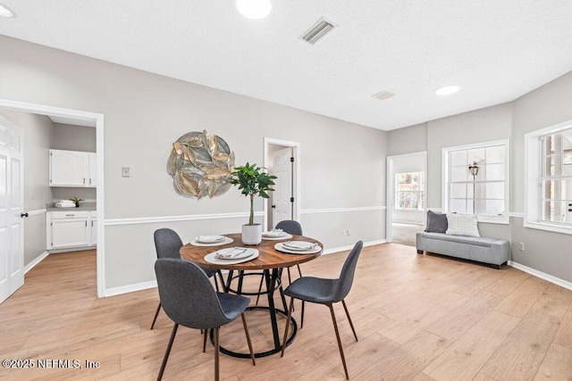 dining room with baseboards, visible vents, light wood finished floors, and a textured ceiling