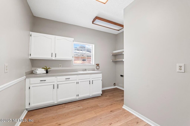 kitchen featuring a sink, light wood-type flooring, baseboards, and white cabinets