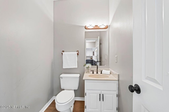 bathroom with toilet, vanity, baseboards, and wood finished floors