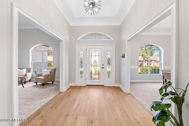 foyer entrance featuring an inviting chandelier, light colored carpet, light wood-type flooring, and ornamental molding