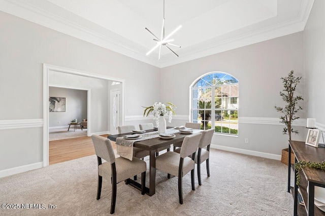 dining space with light colored carpet, baseboards, a raised ceiling, and an inviting chandelier