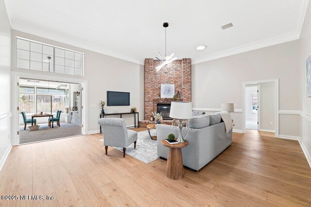 living area with an inviting chandelier, light wood-style flooring, a brick fireplace, and crown molding