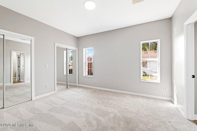 unfurnished bedroom featuring a textured ceiling, multiple windows, baseboards, and light carpet