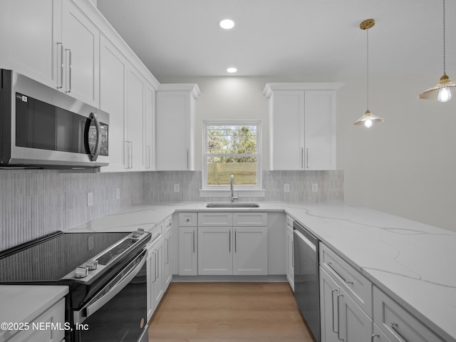 kitchen with light wood finished floors, a sink, white cabinets, appliances with stainless steel finishes, and tasteful backsplash