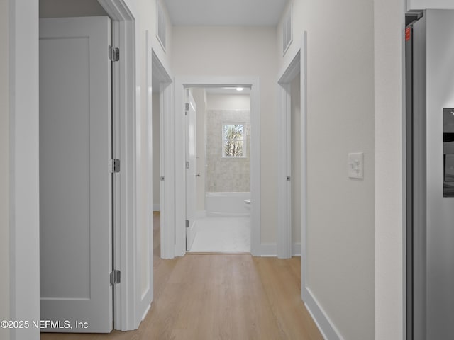 hall featuring visible vents, baseboards, and light wood-style flooring