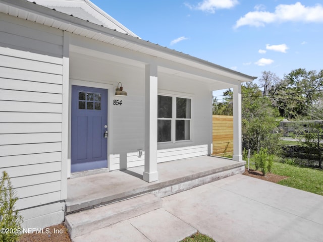 doorway to property with metal roof, a porch, and fence