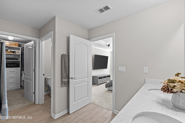 bathroom with wood finished floors, visible vents, a textured ceiling, a walk in closet, and toilet