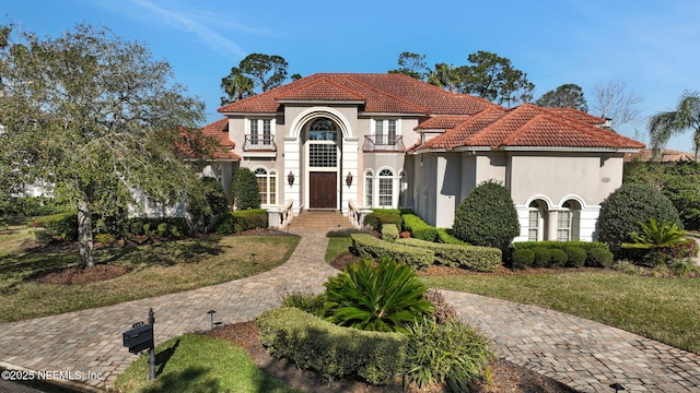 mediterranean / spanish-style house featuring a tile roof, stucco siding, a front yard, and a balcony