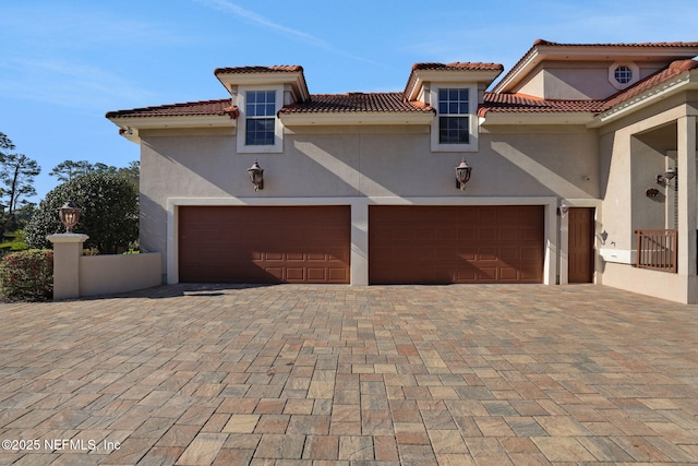 mediterranean / spanish house with a tiled roof, decorative driveway, an attached garage, and stucco siding