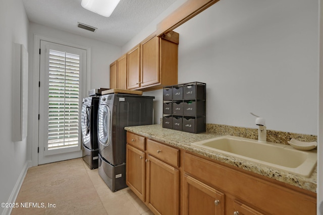 clothes washing area with visible vents, cabinet space, a sink, a textured ceiling, and washing machine and dryer