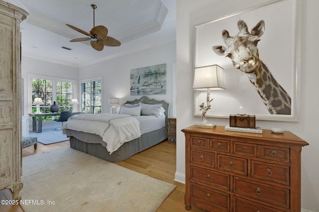 bedroom featuring visible vents, crown molding, a tray ceiling, light wood-style floors, and a ceiling fan