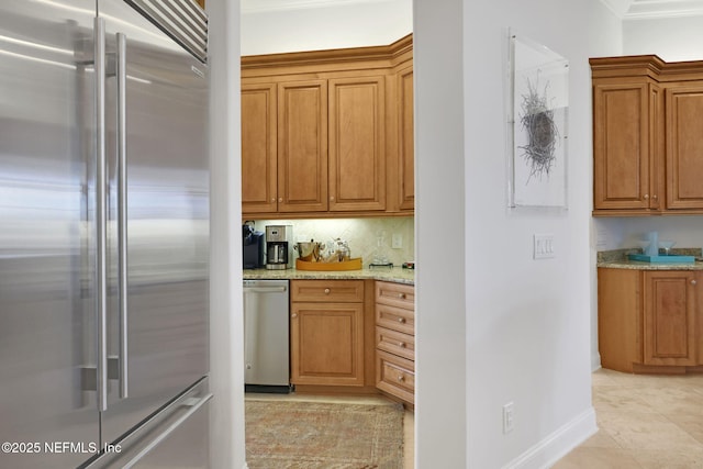 kitchen with stainless steel appliances, brown cabinetry, light tile patterned floors, decorative backsplash, and light stone countertops