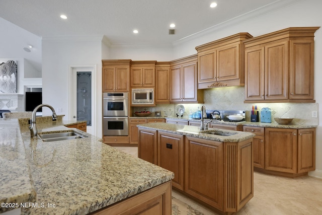 kitchen with appliances with stainless steel finishes, light stone countertops, an island with sink, and a sink