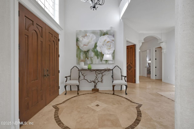 entrance foyer with marble finish floor, arched walkways, decorative columns, baseboards, and a towering ceiling