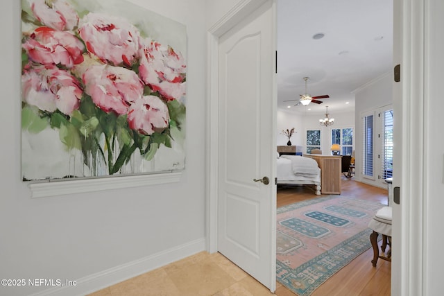 hall featuring crown molding, baseboards, and a chandelier