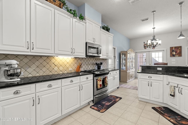 kitchen with dark countertops, visible vents, appliances with stainless steel finishes, light tile patterned flooring, and white cabinets