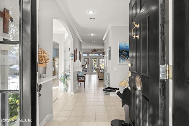 entrance foyer with crown molding, light tile patterned floors, arched walkways, and visible vents