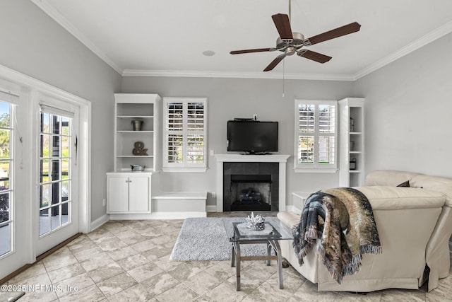 living area with a tiled fireplace, a ceiling fan, baseboards, and ornamental molding