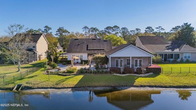 back of house with solar panels, a fenced backyard, french doors, a water view, and a lawn