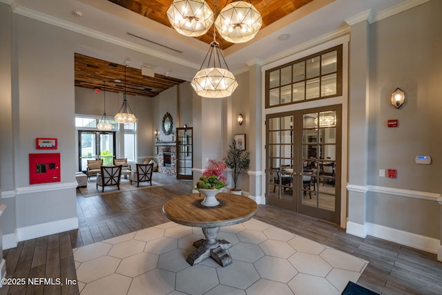 interior space with a tray ceiling, wood finished floors, french doors, a stone fireplace, and crown molding