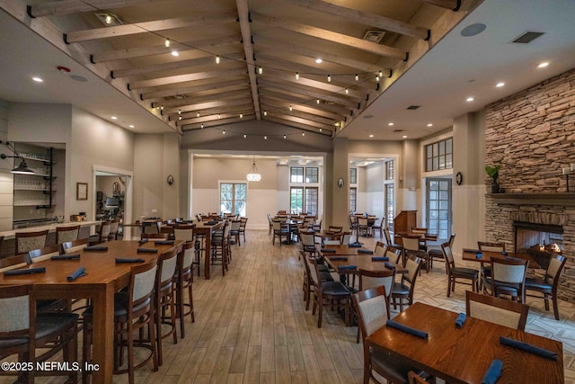 dining room with beamed ceiling, visible vents, high vaulted ceiling, wood finished floors, and a fireplace