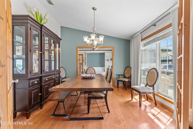 dining space with visible vents, light wood-style floors, an inviting chandelier, and vaulted ceiling