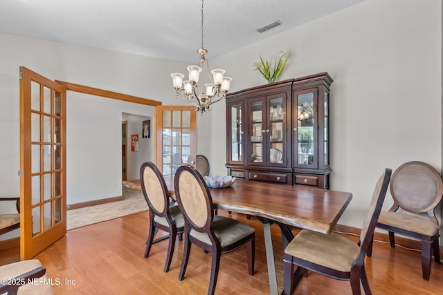 dining area with visible vents, baseboards, a chandelier, french doors, and light wood-style floors