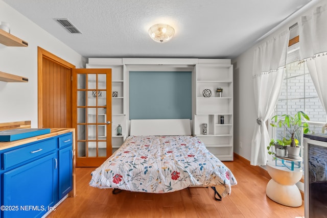 bedroom featuring light wood-style floors, visible vents, and a textured ceiling