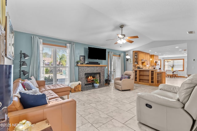 living room with a ceiling fan, visible vents, vaulted ceiling, a tiled fireplace, and marble finish floor