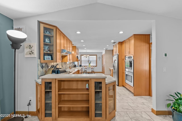 kitchen with under cabinet range hood, stainless steel appliances, light countertops, glass insert cabinets, and a chandelier