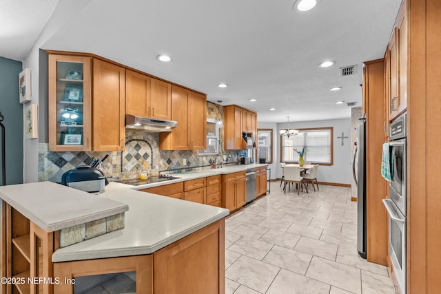 kitchen featuring a peninsula, stainless steel appliances, light countertops, under cabinet range hood, and tasteful backsplash