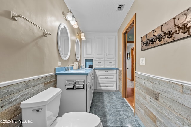 bathroom featuring a wainscoted wall, toilet, vanity, and visible vents