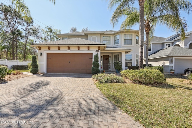 view of front of house featuring a front lawn, fence, stucco siding, decorative driveway, and an attached garage