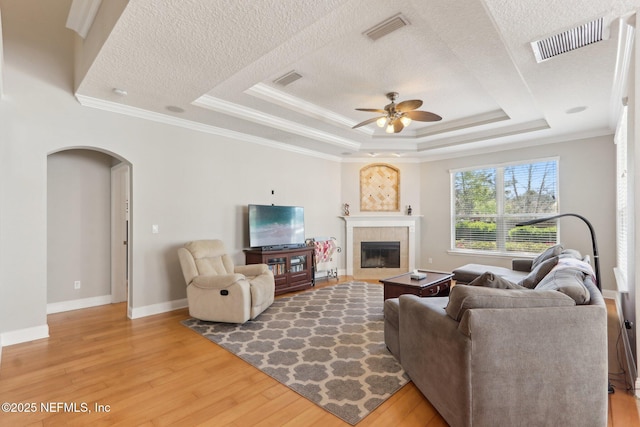 living room featuring a raised ceiling, arched walkways, ceiling fan, and light wood finished floors