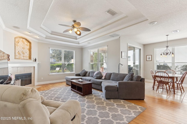 living room with light wood finished floors, visible vents, ceiling fan with notable chandelier, and a raised ceiling