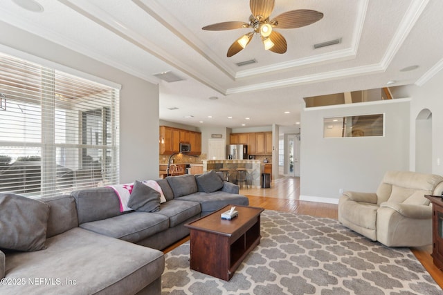 living room featuring visible vents, light wood finished floors, a tray ceiling, ceiling fan, and crown molding