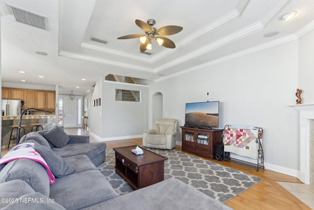 living area featuring a ceiling fan, visible vents, light wood finished floors, a tray ceiling, and arched walkways