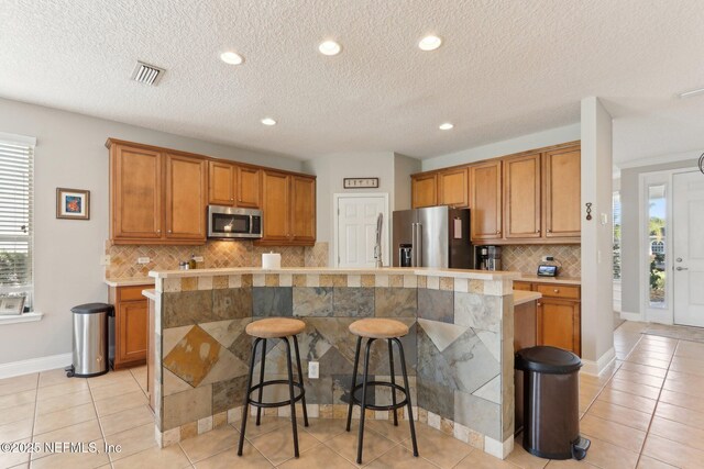 kitchen featuring a kitchen bar, appliances with stainless steel finishes, brown cabinetry, and light countertops