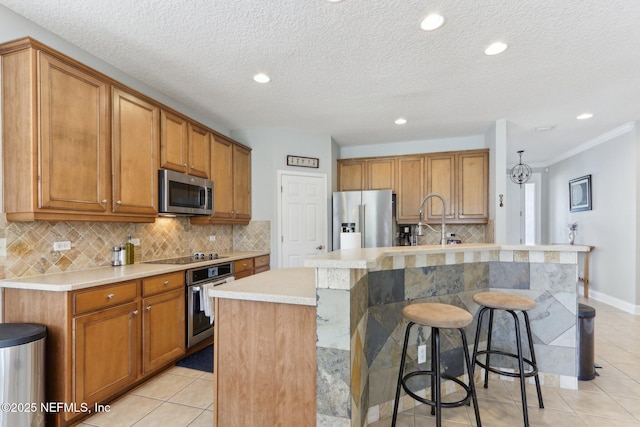 kitchen featuring a center island with sink, a kitchen breakfast bar, appliances with stainless steel finishes, light countertops, and light tile patterned floors