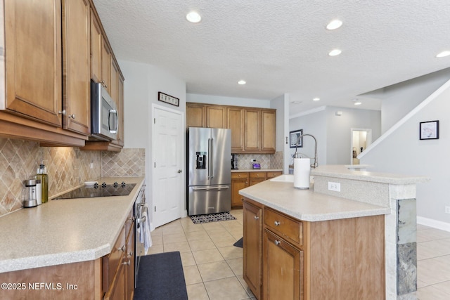 kitchen featuring brown cabinetry, light tile patterned floors, appliances with stainless steel finishes, and a kitchen island with sink