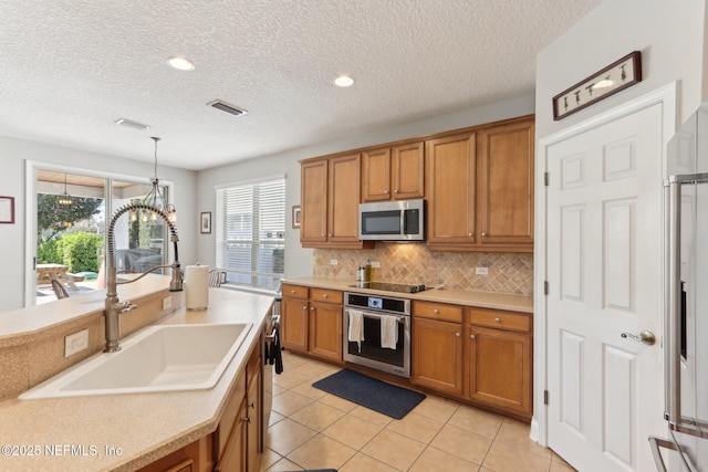 kitchen with visible vents, a sink, appliances with stainless steel finishes, brown cabinetry, and decorative backsplash