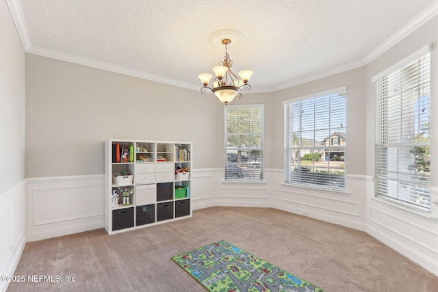 rec room featuring a wainscoted wall, a notable chandelier, a textured ceiling, crown molding, and carpet flooring